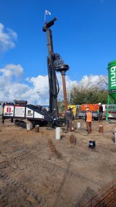 Bohrgerät führt Tiefbohrarbeiten für Fundament durch auf Baustelle mit LKW und Bauarbeitern